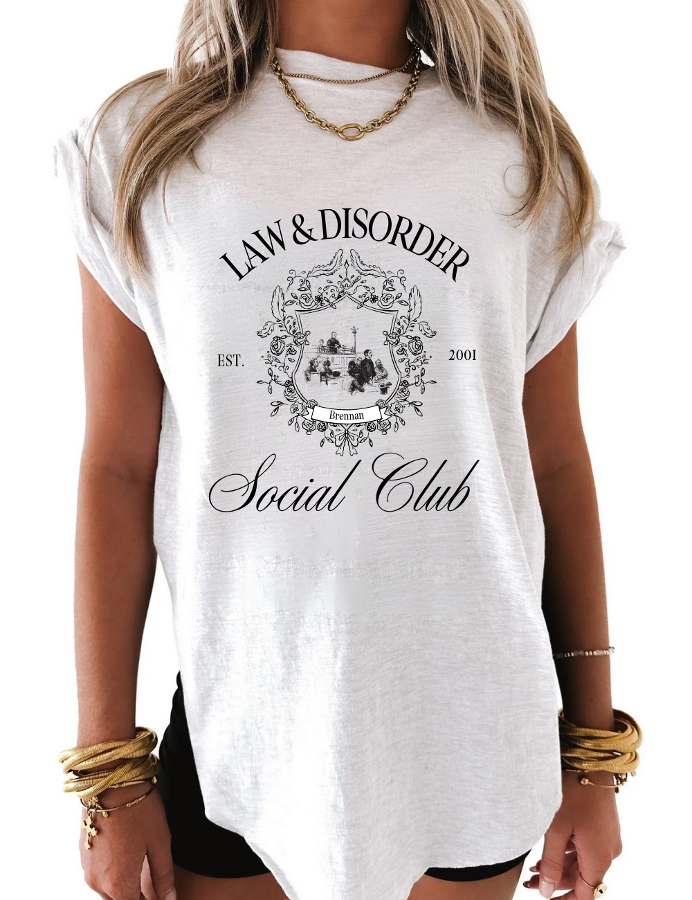 Flat lay of white graphic tee that says “Law and Disorder” in bold black letters, folded on neutral background with chain-link accessories, Gen Z fashion.